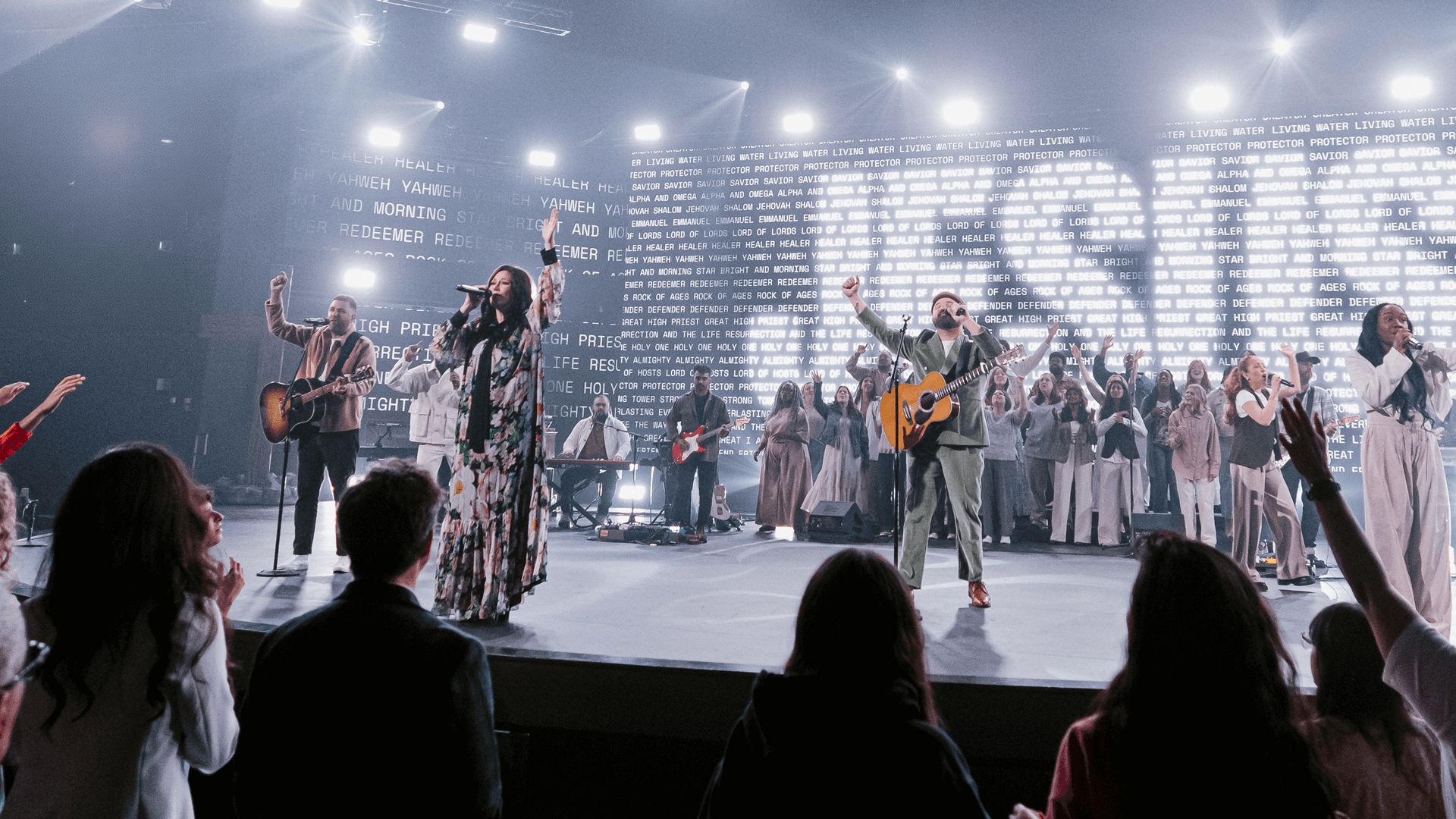 People worshipping on stage with the name Jesus behind